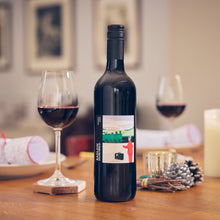 Load image into Gallery viewer, Rondo an Englush Wine stands on a wooden table beside a filled wine glass, with blurred candles, plates, and framed wall art in the background.