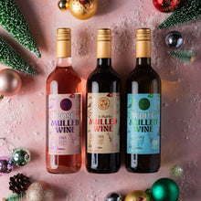 Load image into Gallery viewer, Three bottles of Christmas mulled wine arranged on a pink surface with festive ornaments and mini green trees. 
