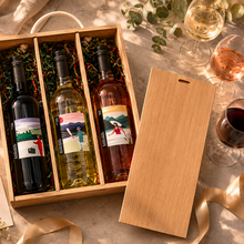 Load image into Gallery viewer, Three wine bottles in a wooden gift box with glasses and ribbons on a table.
