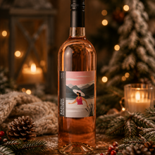 Load image into Gallery viewer, A bottle of Radlow Hundred Rosé wine with a festive holiday label, styled on a rustic wooden surface with pine branches, pinecones, and warm bokeh lights in the background.
